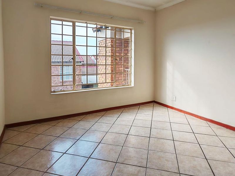 A bright, empty bedroom featuring neutral tiled flooring, clean walls, and a large window fitted with security bars.