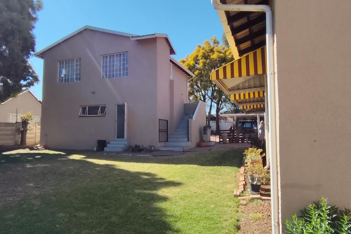 Rear view of the property featuring a lawn, external staircase, and a covered patio area with striped awnings.