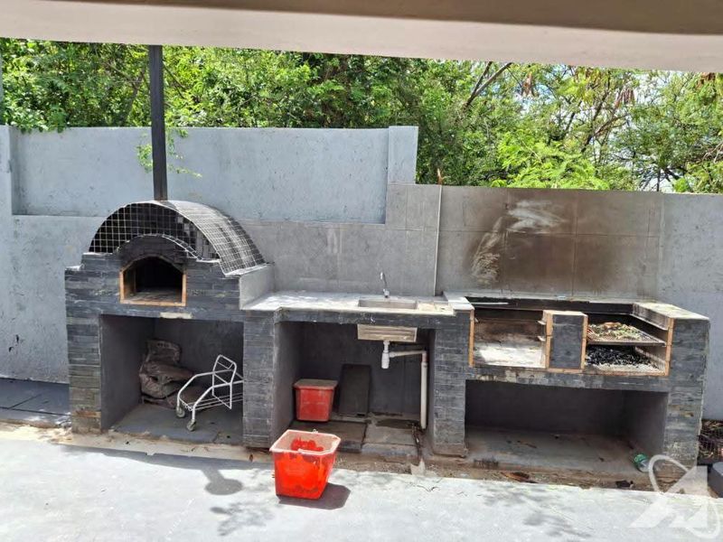 Outdoor entertainment area featuring a built-in pizza oven, masonry braai station, and integrated sink with tiled splashback.
