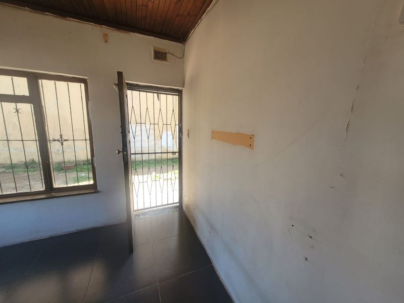 An empty entry area featuring dark tiled flooring, a timber ceiling, and security gates on both the door and window.
