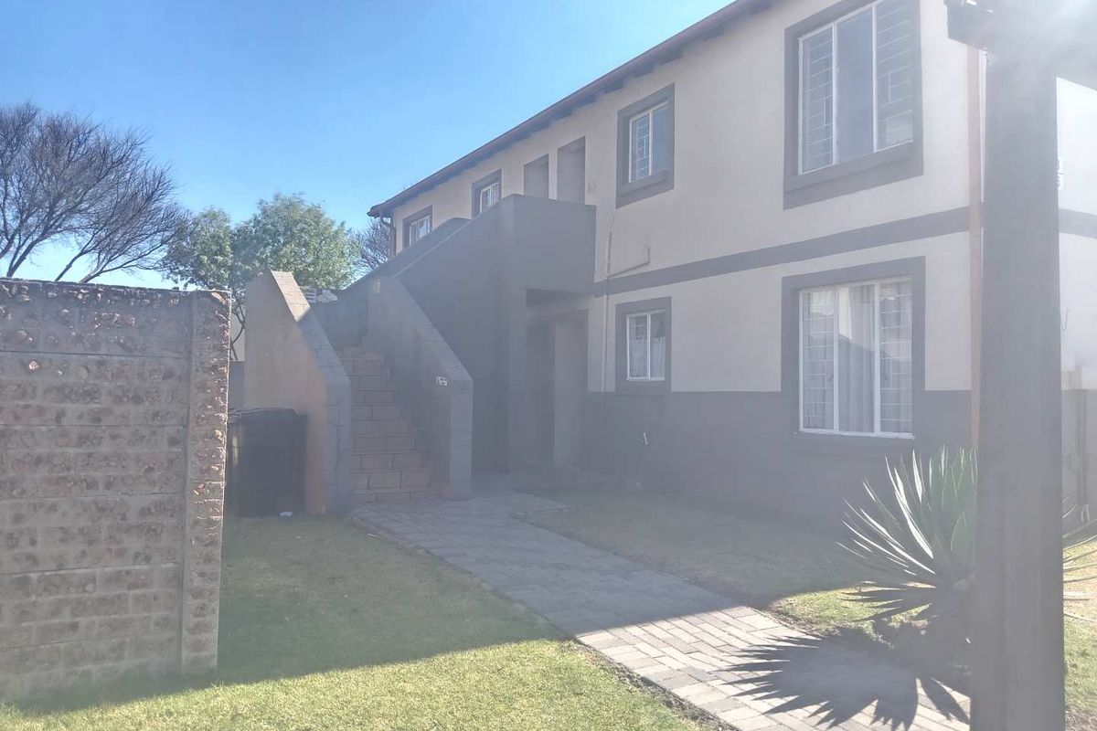 Rear view of a two-story townhouse complex featuring a paved walkway, external staircase, and established garden area.