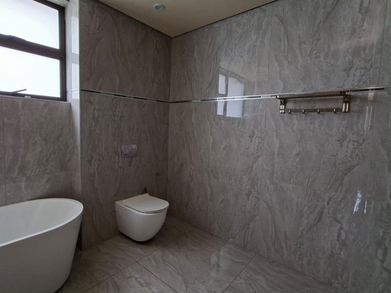 Modern bathroom featuring floor-to-ceiling grey marble-look tiles, a sleek freestanding bathtub, wall-hung toilet with concealed cistern, and a glass-enclosed shower area.
