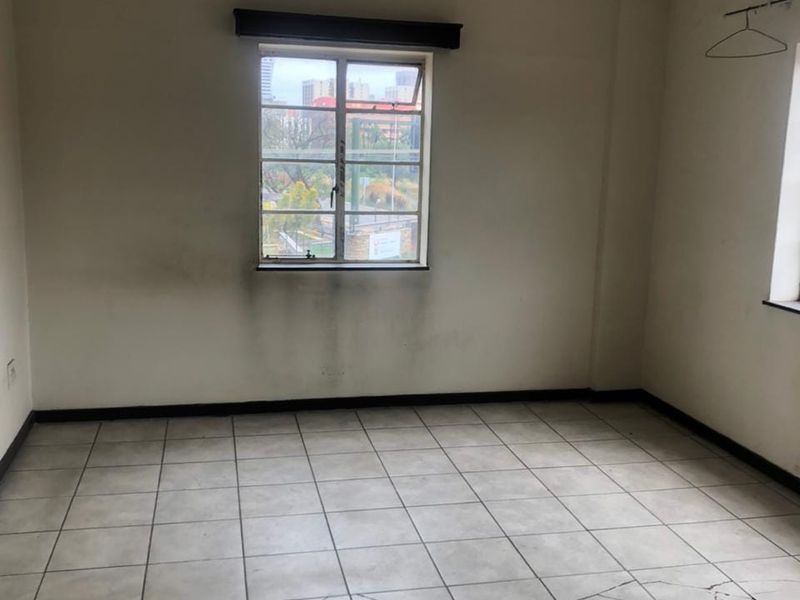 An empty bedroom featuring tiled flooring, casement windows, and a pendant light fixture, requiring cosmetic updates to address wall staining and cracked floor tiles.