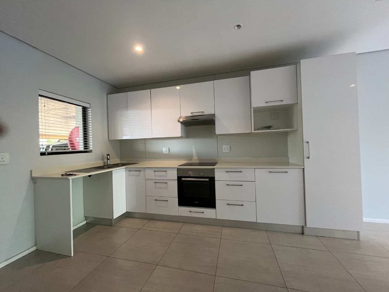Modern kitchen featuring white built-in cabinetry, stone countertops, integrated oven and hob, and tiled flooring in a clean, minimalist layout.