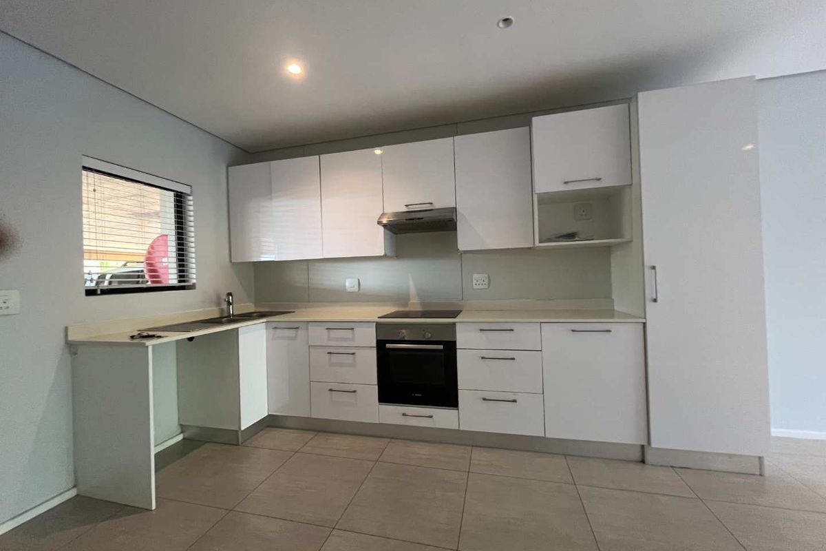 Modern kitchen featuring white built-in cabinetry, stone countertops, integrated oven and hob, and tiled flooring in a clean, minimalist layout.