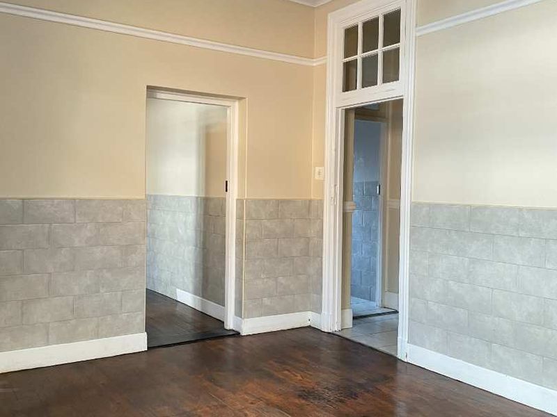 An empty living area featuring original hardwood flooring, decorative wainscoting, and classic architectural detailing around the doorways.