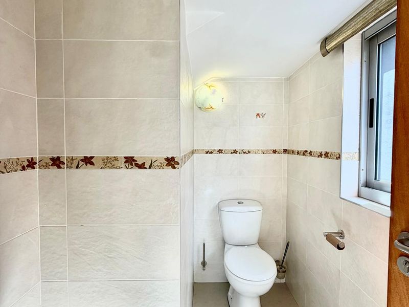 A compact, tiled bathroom featuring a standard toilet, neutral wall tiles with a decorative border, and a small window for natural light.