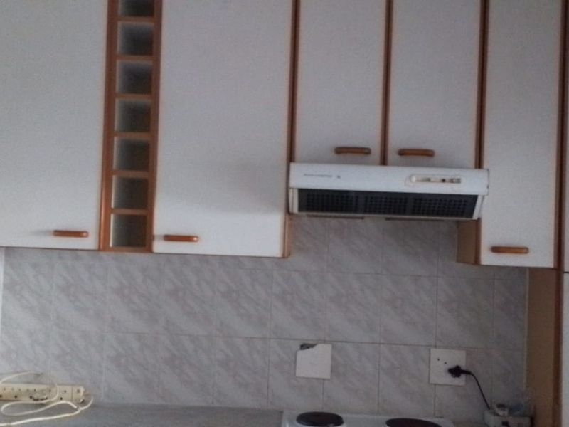 A dated kitchen area featuring white built-in cabinetry, a tiled backsplash, and an integrated extractor fan above the electric hob.