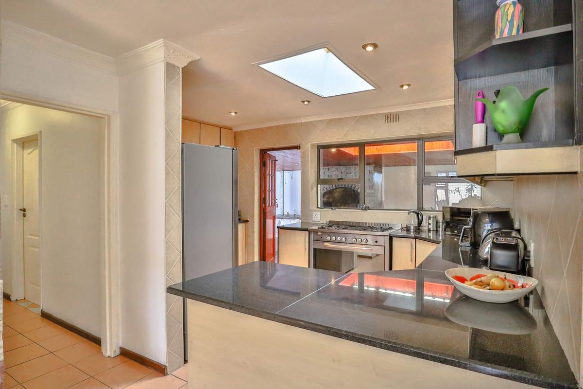 A functional kitchen featuring dark granite countertops, built-in oven and hob, and a skylight providing natural light, with an adjacent hallway.