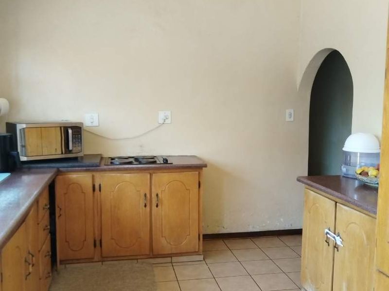 A functional kitchen featuring wooden cabinetry, laminate countertops, a built-in gas hob, and tiled flooring, accessible via an arched doorway.