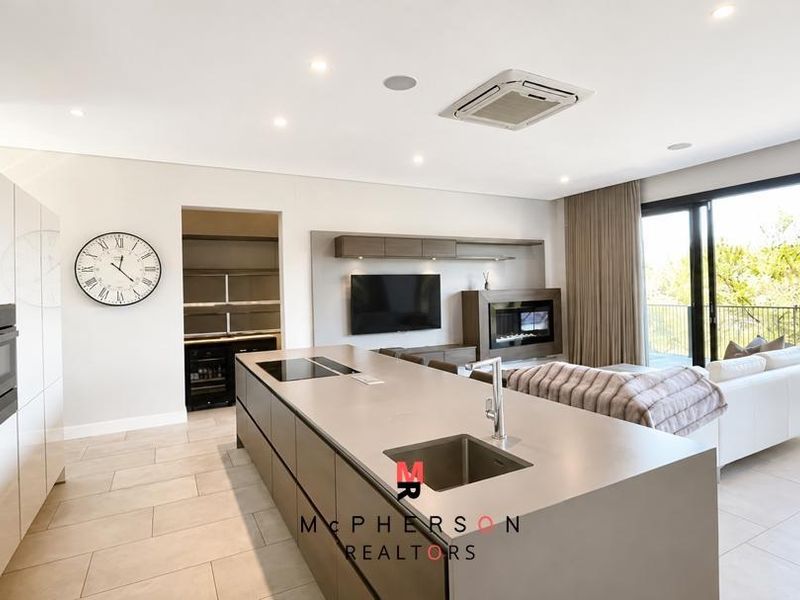 Modern open-plan living area featuring a sleek kitchen island, integrated appliances, built-in fireplace, and seamless access to an outdoor balcony.