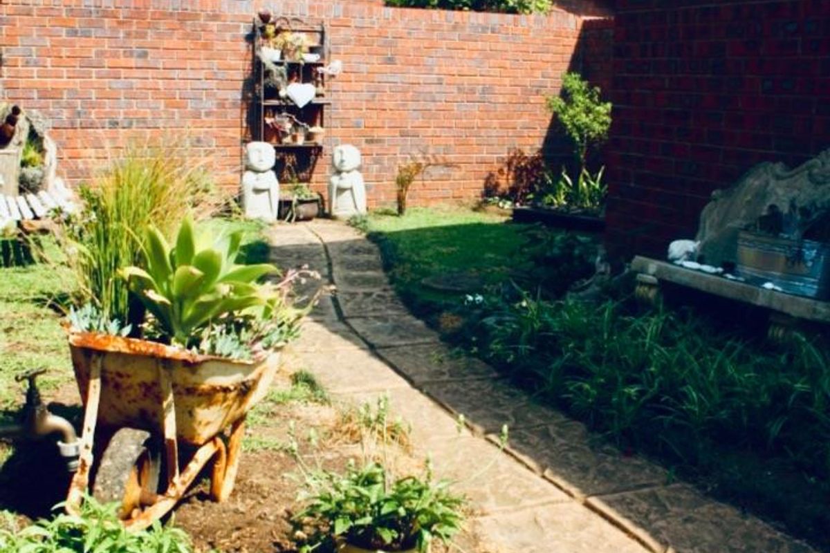 A private rear courtyard featuring a paved walkway, brick boundary walls, and established garden beds in a townhouse setting.