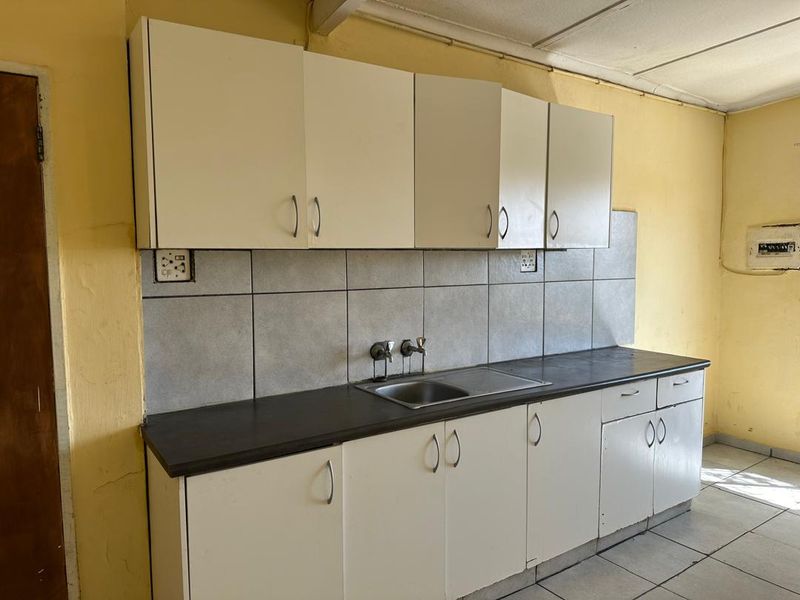 A functional kitchen space featuring built-in cabinetry, a stainless steel sink, and tiled backsplash, currently in need of cosmetic updates.