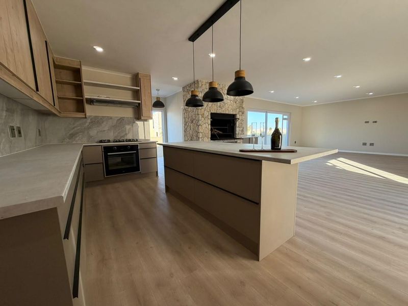 Modern open-plan kitchen featuring a central island, stone-clad fireplace, and high-quality finishes, seamlessly flowing into a spacious living area.