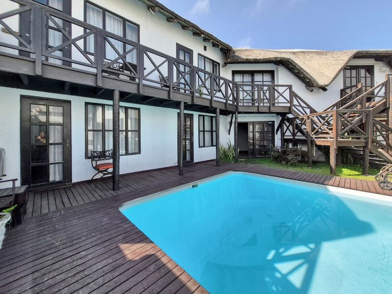 Outdoor pool area featuring timber decking, a thatched roof structure, and a wooden balcony with staircase access to the upper level.