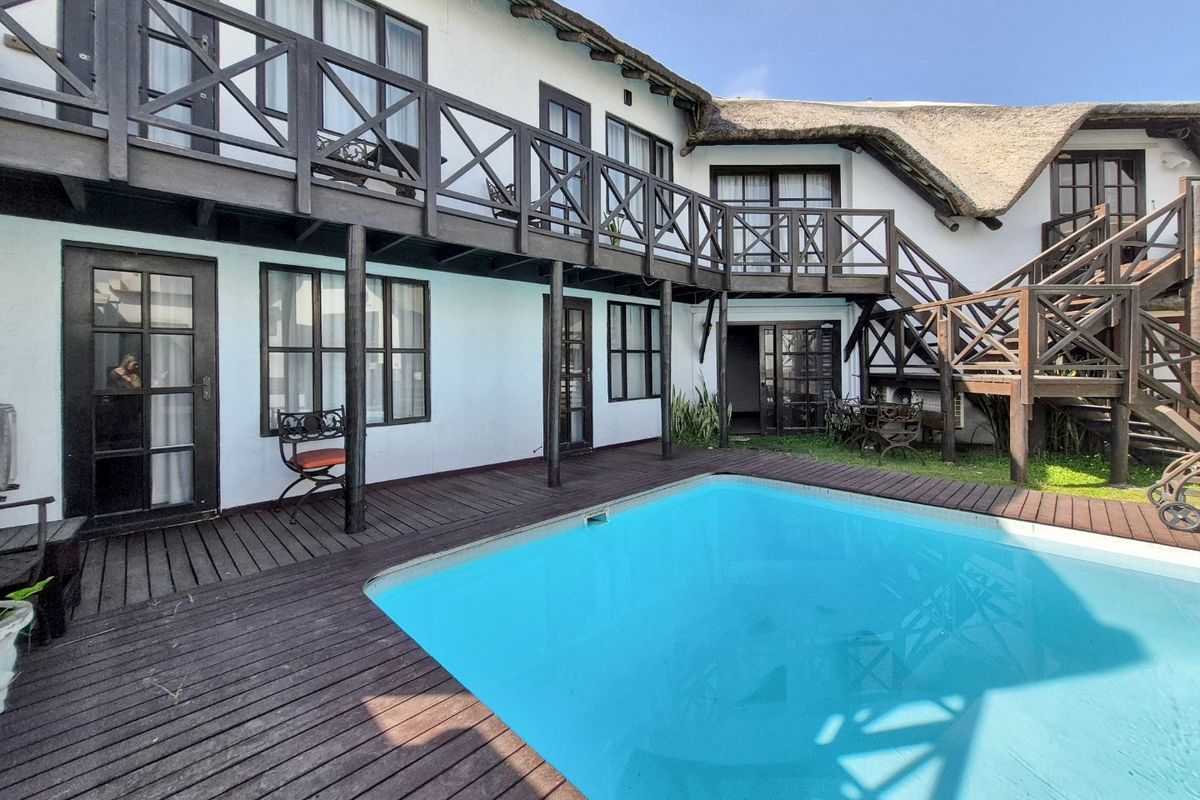 Outdoor pool area featuring timber decking, a thatched roof structure, and a wooden balcony with staircase access to the upper level.