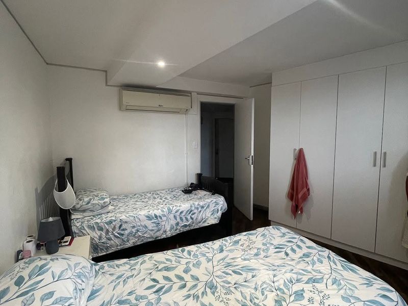 A functional bedroom featuring built-in cupboards, timber flooring, and a wall-mounted air conditioning unit.