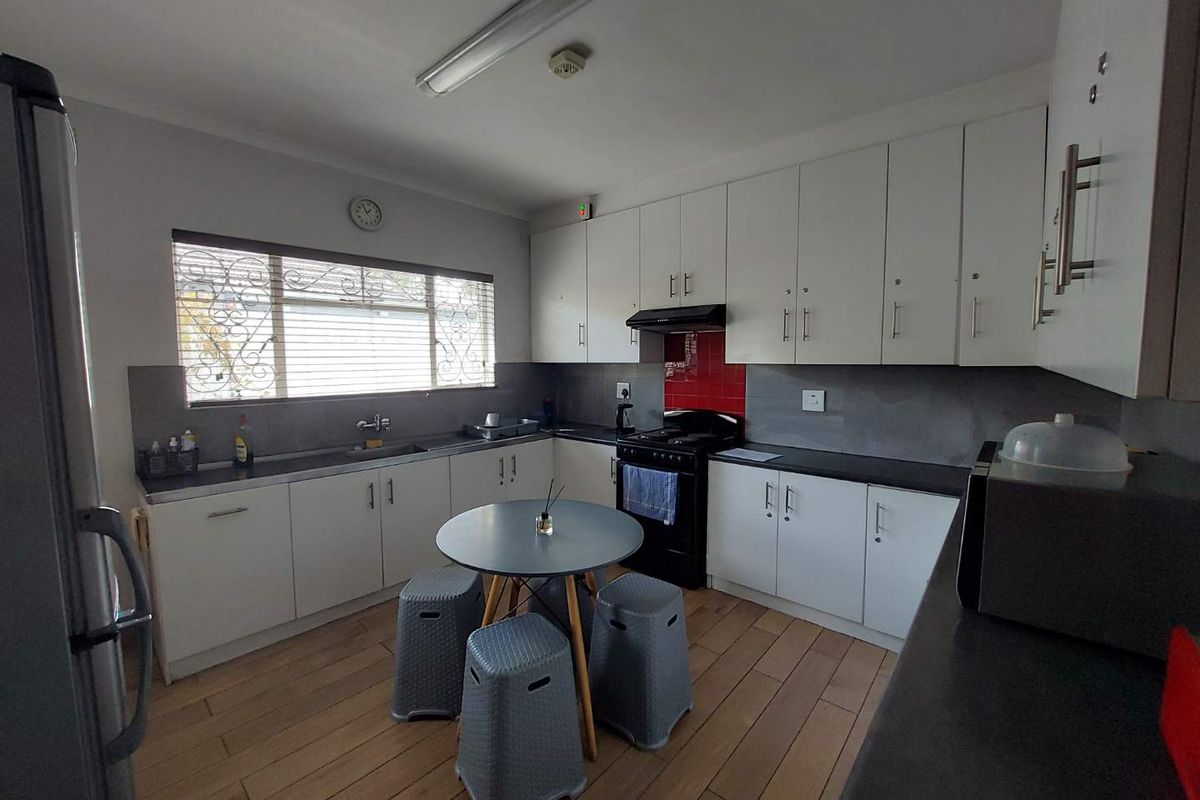 A functional office kitchen featuring white cabinetry, dark countertops, a built-in stove with extractor fan, and wood-look flooring.