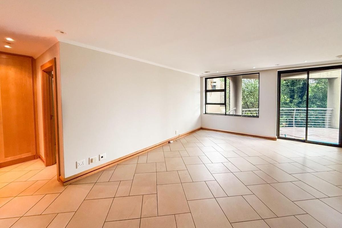 A spacious, light-filled living area featuring neutral tiled flooring, recessed downlighting, and large sliding glass doors that open onto an outdoor balcony.