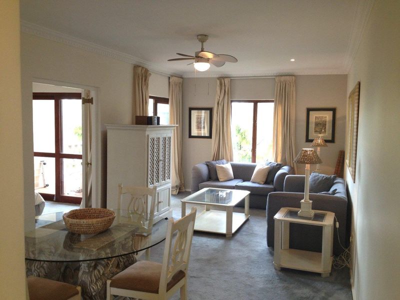 A comfortable living room featuring crown molding, a ceiling fan, and access to an outdoor area through double glass doors.
