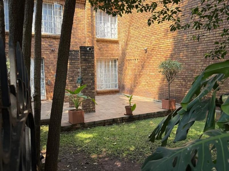 A private rear courtyard featuring a paved patio area, established brick townhouse facade, and a small garden space.