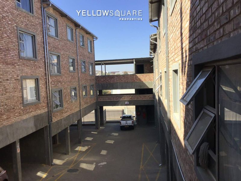 Exterior view of an apartment complex featuring exposed brick facades, casement windows, and a covered ground-level parking area.