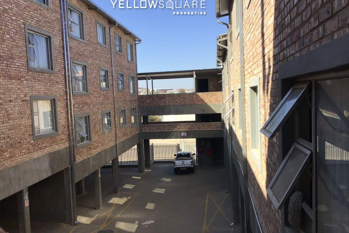 Exterior view of an apartment complex featuring exposed brick facades, casement windows, and a covered ground-level parking area.
