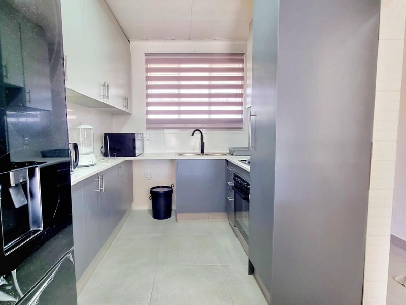 A modern, compact kitchen featuring grey and white cabinetry, built-in oven, hob, and a double sink with a contemporary black mixer tap.