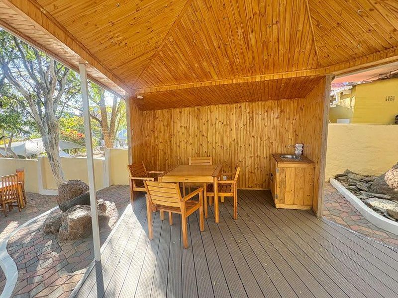 A covered outdoor patio area featuring timber-clad walls and ceiling, composite decking, and a built-in kitchenette unit with a sink.