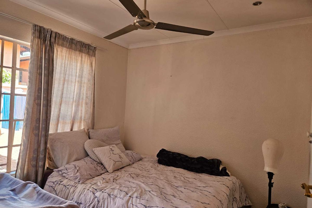 A standard bedroom featuring a ceiling fan, recessed lighting, and natural light through a window with curtain rails.