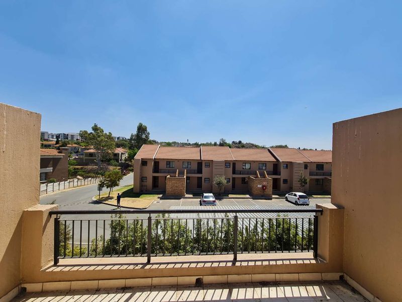 An elevated balcony with a metal balustrade offering an open view of the apartment complex grounds and parking area.