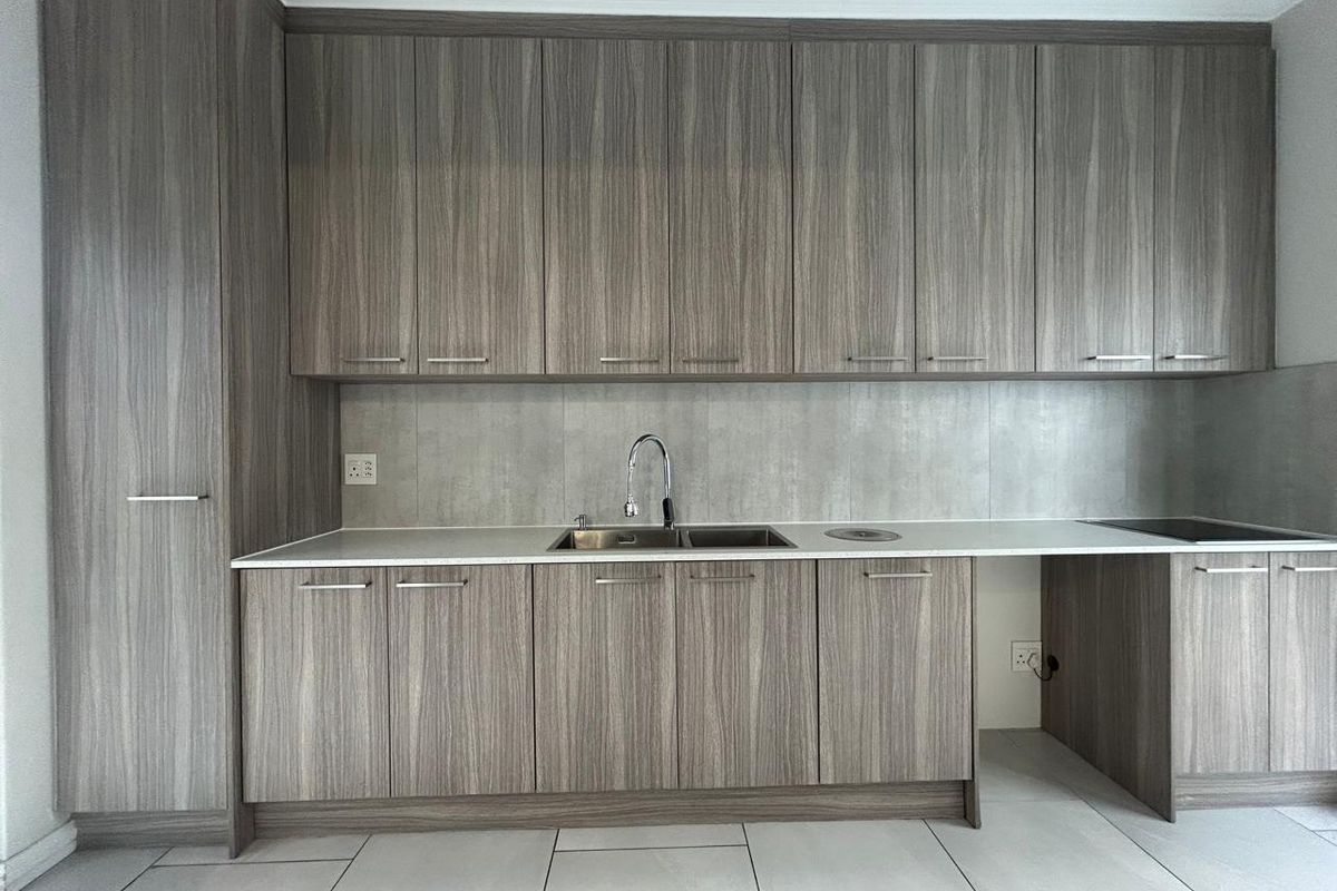 Modern kitchen featuring wood-grain cabinetry, stone countertops, a stainless steel sink, and tiled flooring in a clean, minimalist layout.