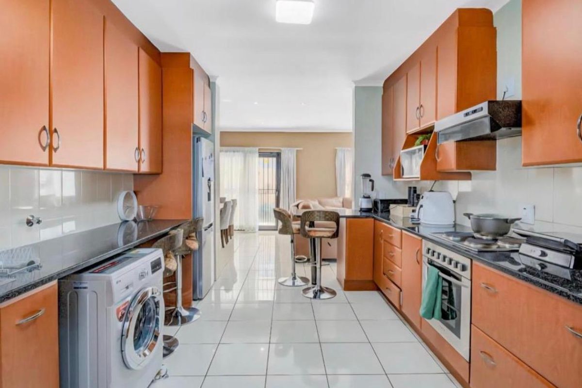 A functional galley-style kitchen featuring wood-finish cabinetry, granite countertops, a built-in oven with hob, and an integrated laundry space.