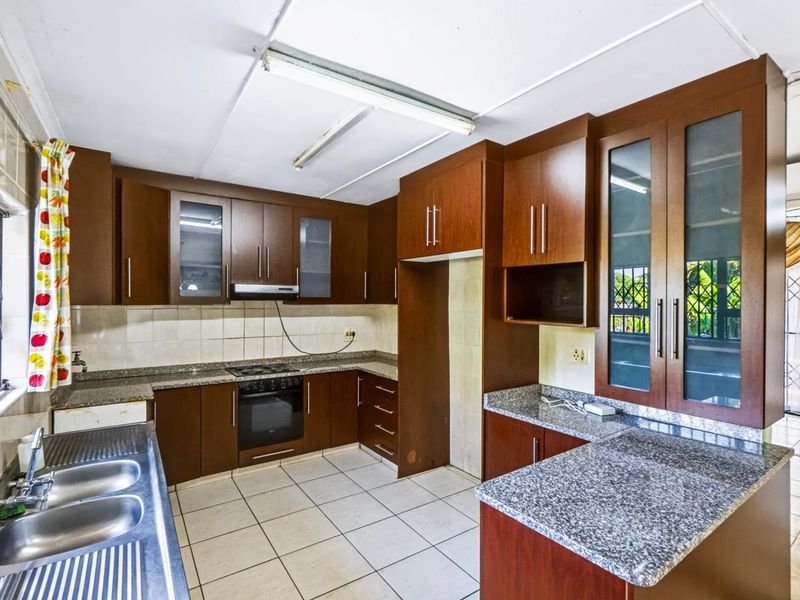 A functional kitchen featuring dark wood cabinetry, granite countertops, a built-in oven and hob, and tiled flooring with security bars on the windows.