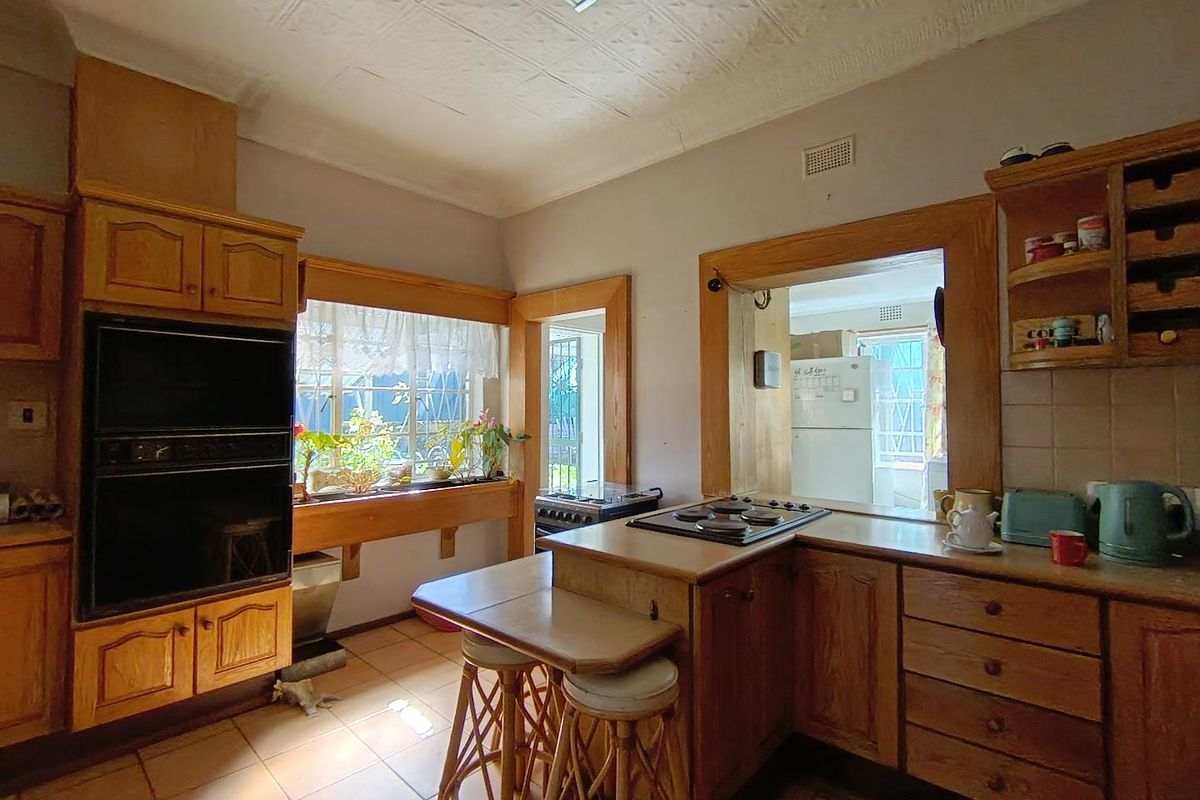 A dated kitchen featuring wooden cabinetry, built-in oven, electric hob, and a unique pressed metal ceiling with a convenient pass-through window.