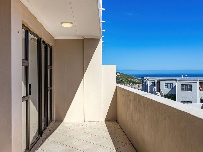 A clean, covered balcony featuring tiled flooring and sliding glass door access, offering clear views of the surrounding neighborhood and the ocean.