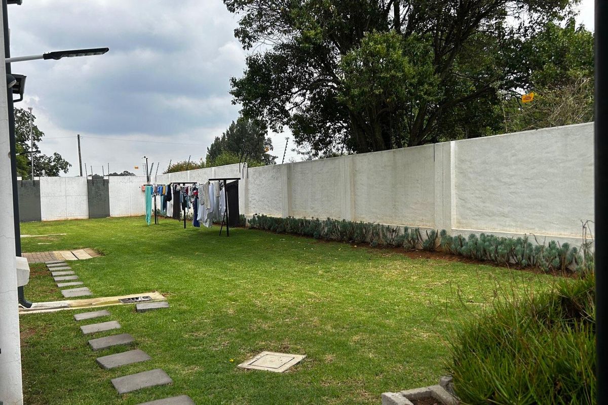 A private rear garden featuring a well-maintained lawn, stone paver pathway, and a secure perimeter boundary wall with integrated electric fencing.