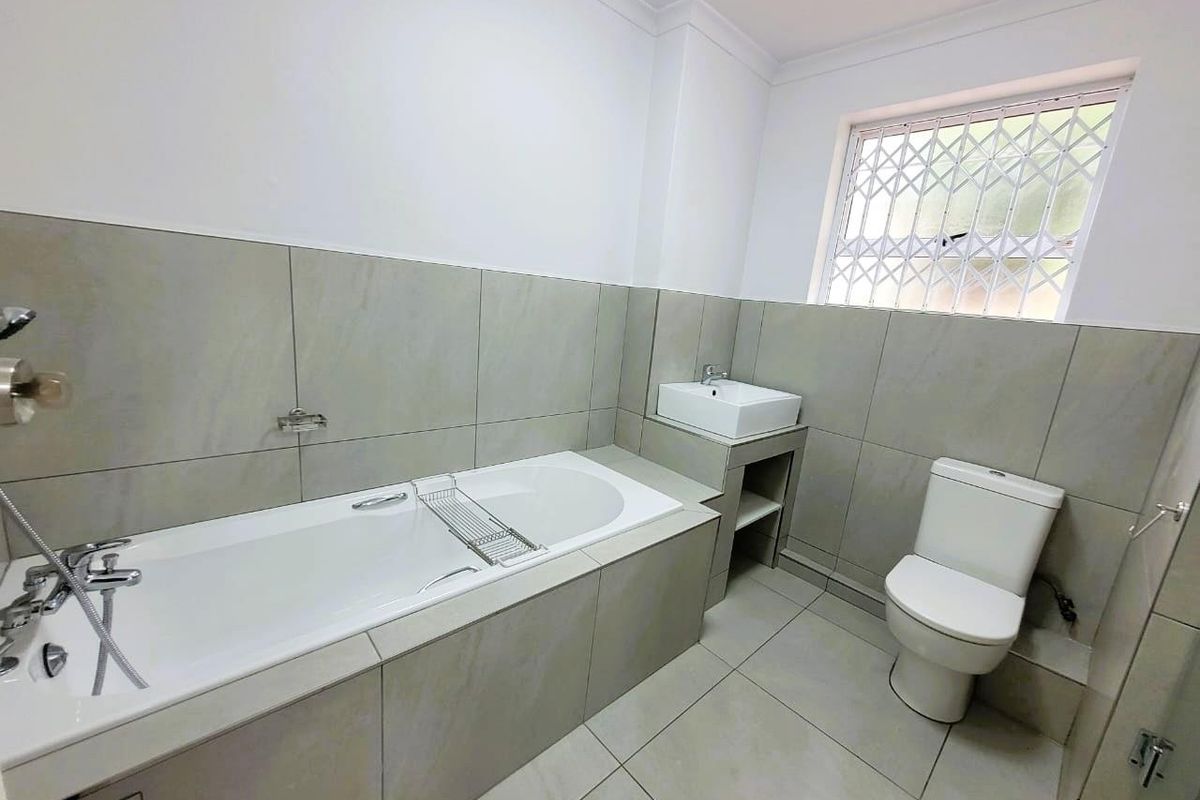 Modern bathroom featuring large format wall and floor tiles, a built-in bathtub with chrome fixtures, a vessel sink, and a toilet.