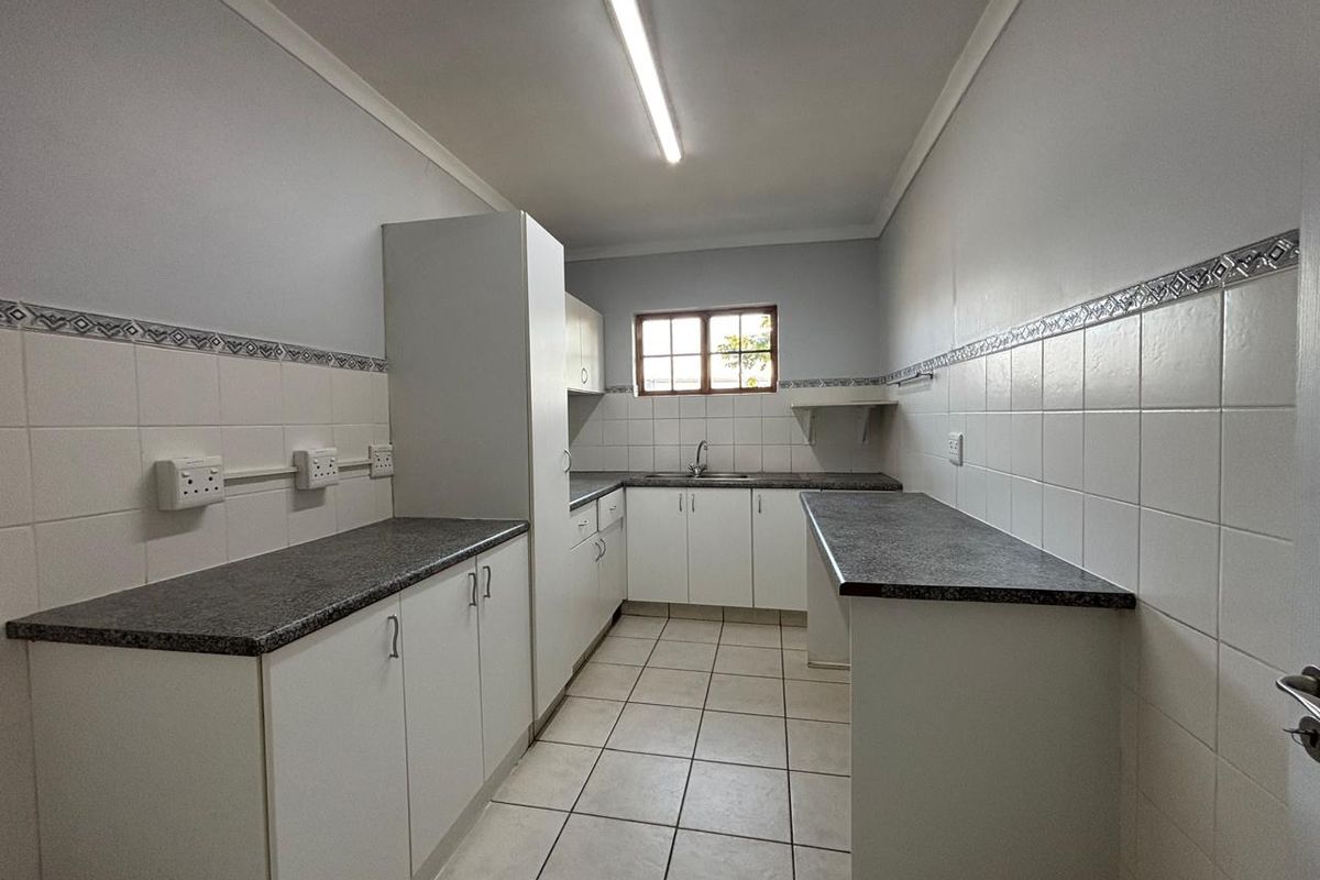 A functional kitchen area featuring white cabinetry, dark laminate countertops, tiled flooring, and a single basin sink with a window for natural light.