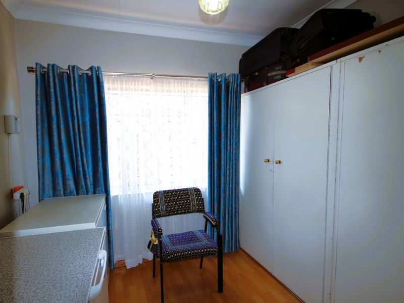A bedroom featuring laminate flooring, built-in cupboards, and a window with curtains.