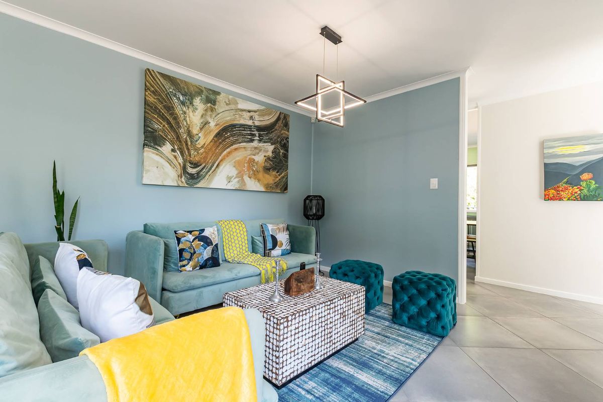 A well-maintained living room featuring modern geometric lighting, neutral tiled flooring, and coved ceilings, creating a bright and inviting atmosphere.