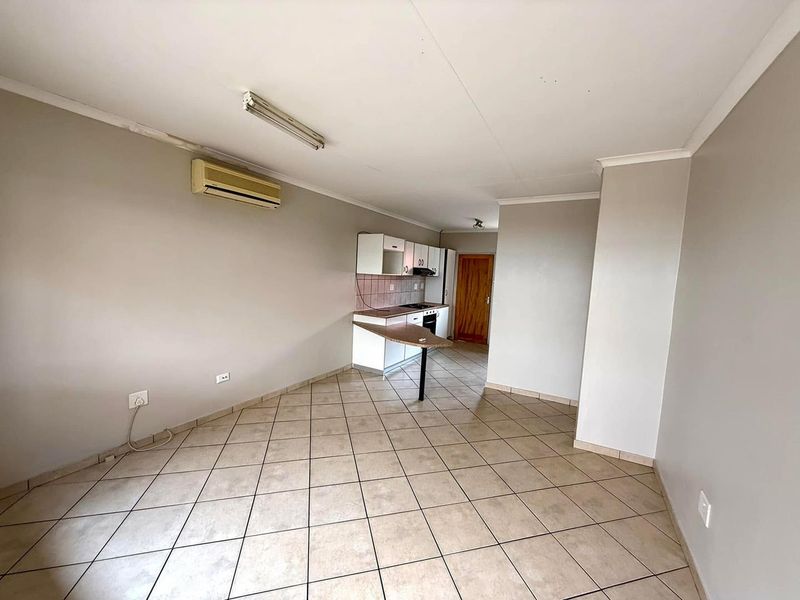 Open-plan living area featuring tiled flooring, a split-system air conditioner, and a compact kitchen with built-in cabinetry and appliances.