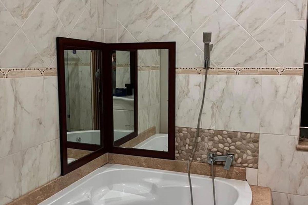 A corner bathtub featuring marble-look wall tiles, a stone-tiled accent border, and a handheld shower fixture.