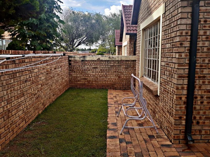 A private rear courtyard featuring a paved patio area, a small lawn, and brick boundary walls with security-fitted windows.