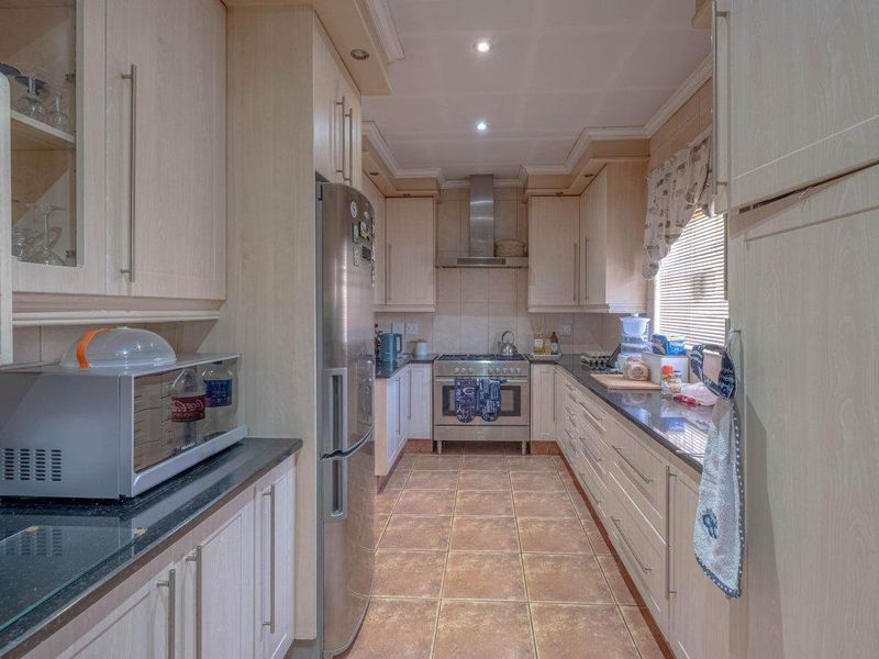 A functional galley-style kitchen featuring light wood-finish cabinetry, dark granite countertops, stainless steel appliances, and tiled flooring with recessed lighting.