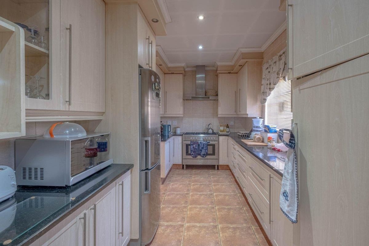 A functional galley-style kitchen featuring light wood-finish cabinetry, dark granite countertops, stainless steel appliances, and tiled flooring with recessed lighting.