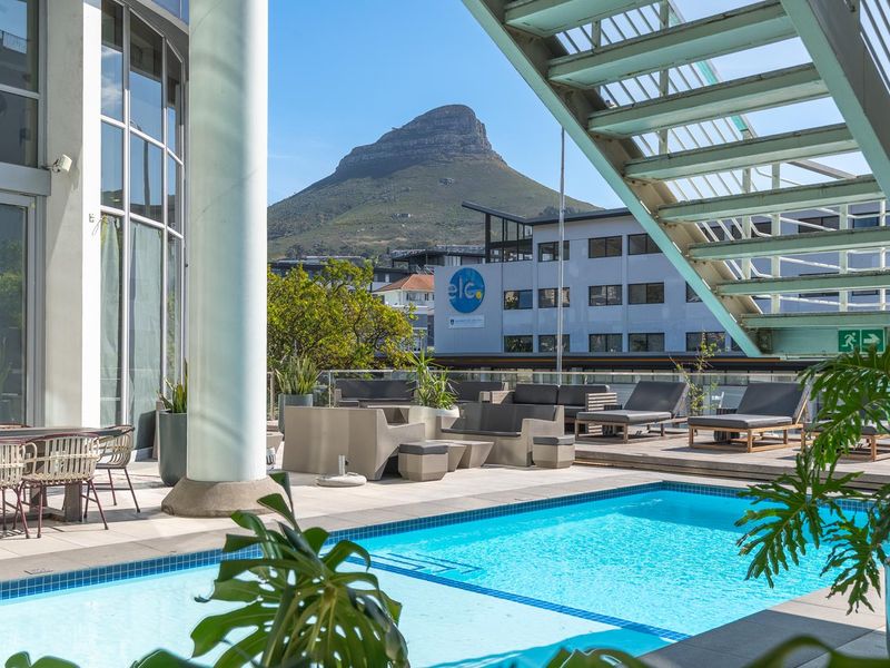 A modern penthouse pool deck featuring a swimming pool, glass balustrades, and a metal staircase, offering stunning mountain views.