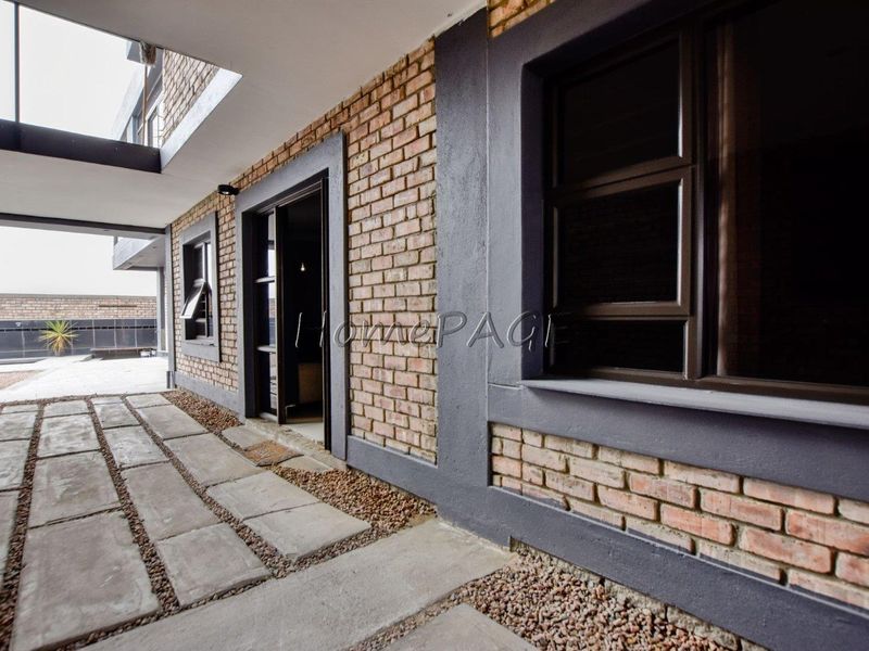 A modern covered patio area featuring exposed brick walls, dark aluminium window frames, and concrete paving with decorative pebble borders.