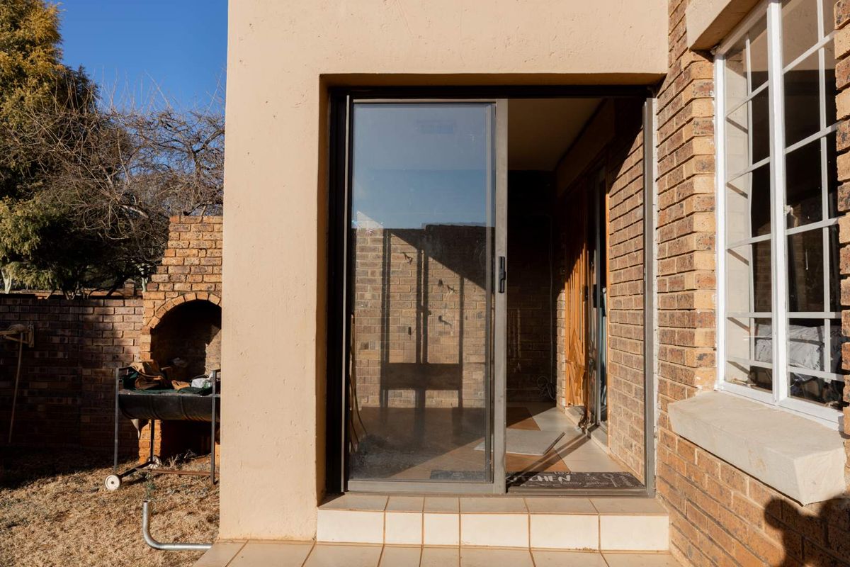 Exterior view of a patio area featuring a built-in brick braai, sliding glass door access, and face-brick wall finishes.