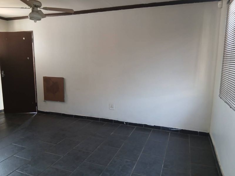 An empty living room featuring dark tiled flooring, a ceiling fan, and venetian blinds, presenting a blank canvas for interior design.